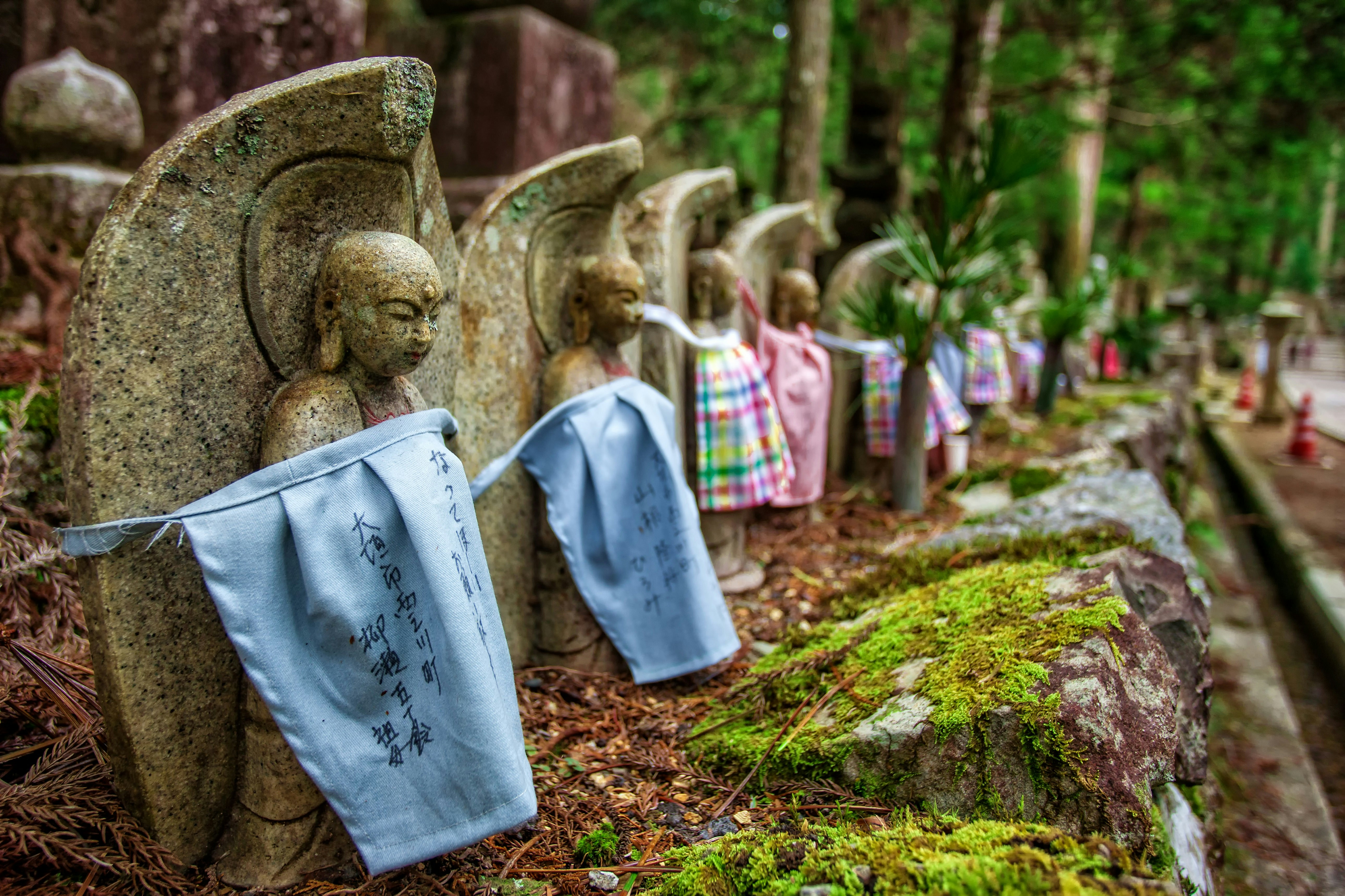 Okunoin Cemetery in Koyasan, Japan. A number of small stone statues are wrapped in fabric, amidst a forest setting.
